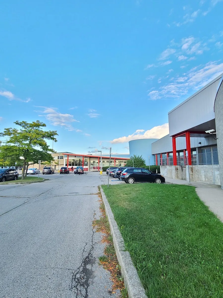 The arena's grey side wall with red columns along the entrance walkway, beside the driveway and parking lot. — Chedoke Twin Pad Arena