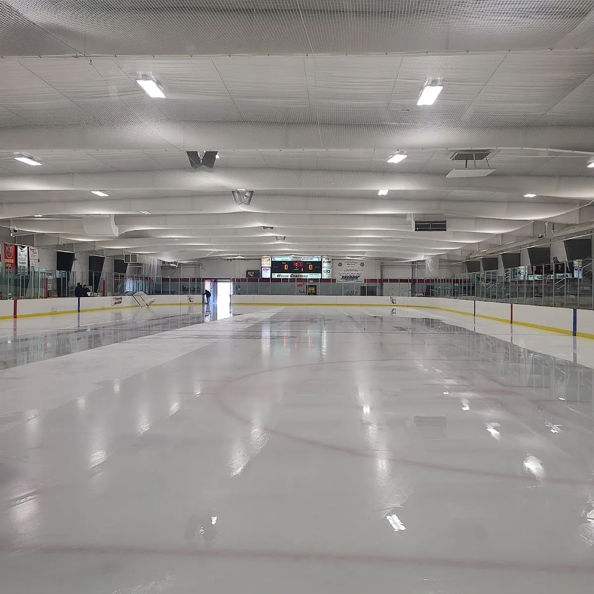 La pista vacía de Cheektowaga Recreation Center Arena, recién inundada bajo un techo blanco con hileras de luces y un marcador en el extremo opuesto. — Cheektowaga Recreation Center Arena
