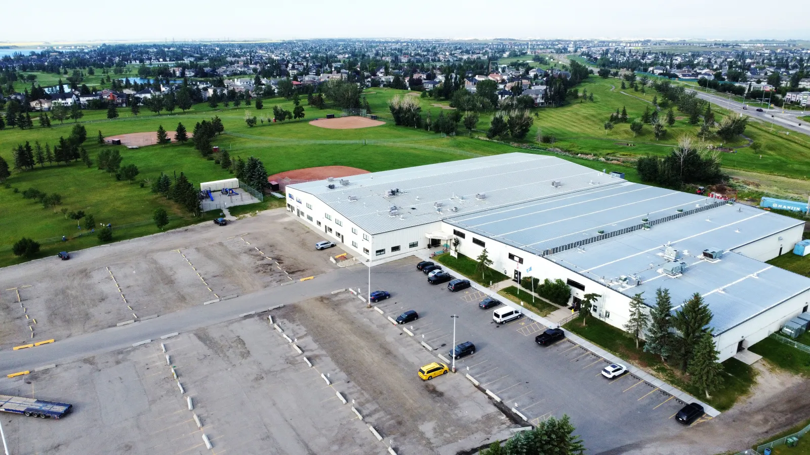Vista aérea del Chestermere Recreation Centre, el largo edificio de techo gris con su estacionamiento, junto al campo de golf y los campos — Chestermere Recreation Centre