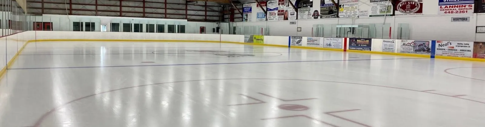The empty ice of the arena with its sponsor boards, which carry Chesterville businesses, and the exposed timber roof structure — Chesterville Arena