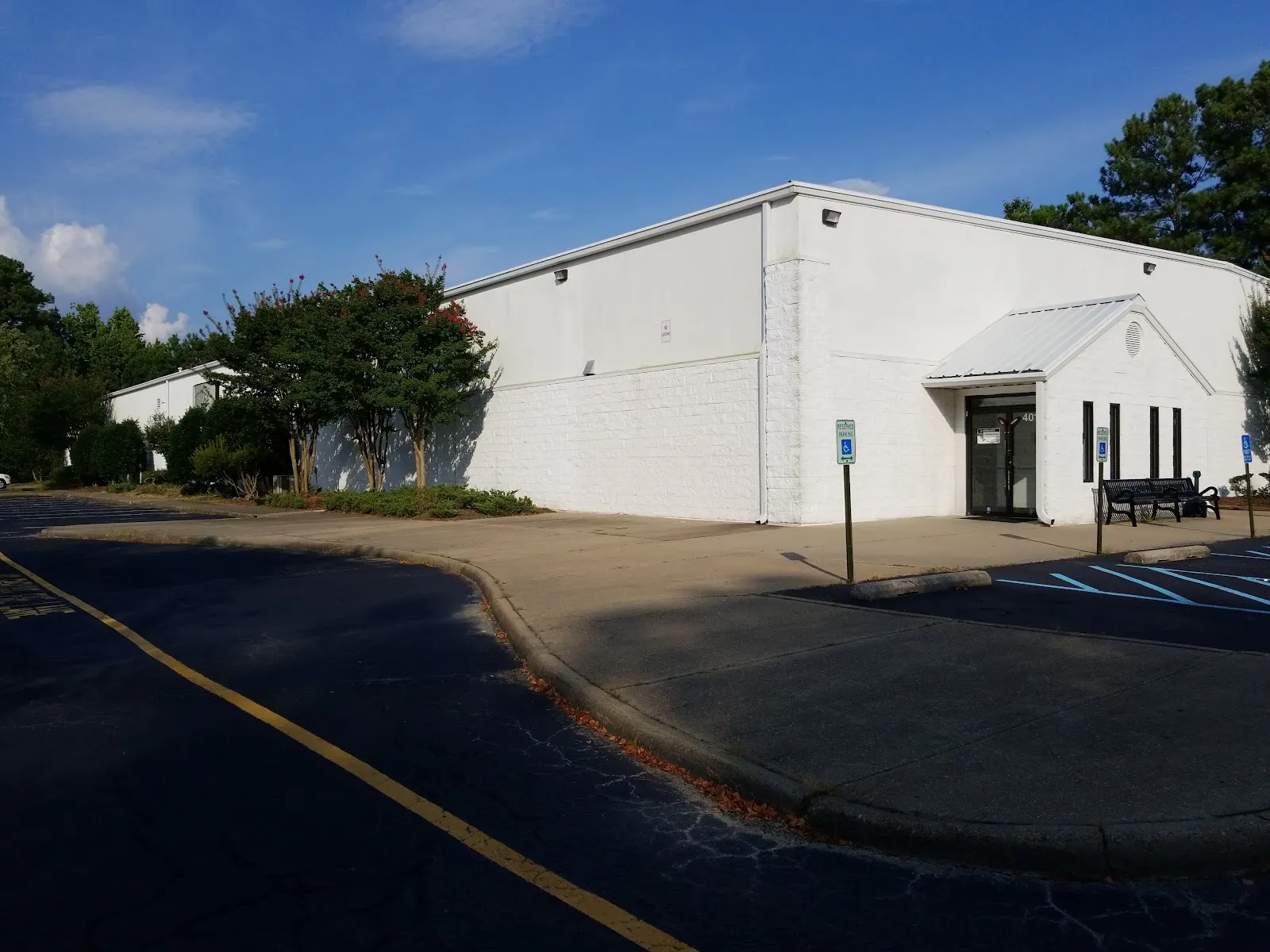 El edificio blanco de la pista de Chilled Ponds at Yorktown con su pequeña entrada a dos aguas, visto al otro lado del estacionamiento en un día despejado — Chilled Ponds at Yorktown (formerly Hampton Roads Iceplex)