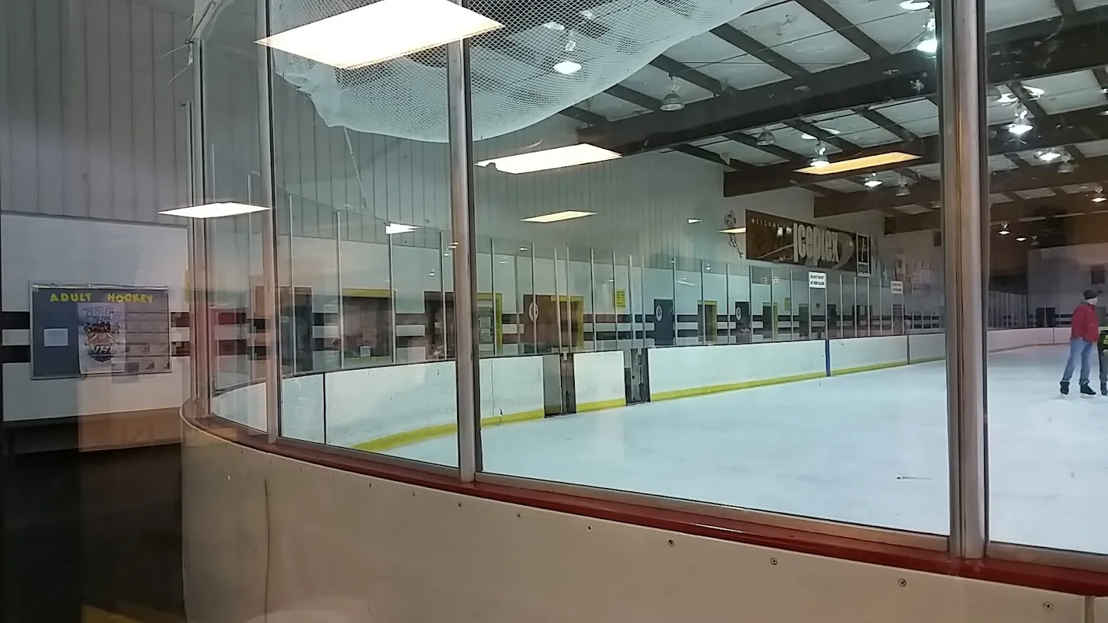 El hielo de Chilled Ponds at Yorktown visto a través del cristal curvo de la pista, con las vallas y la red y un patinador en el borde derecho — Chilled Ponds at Yorktown (formerly Hampton Roads Iceplex)