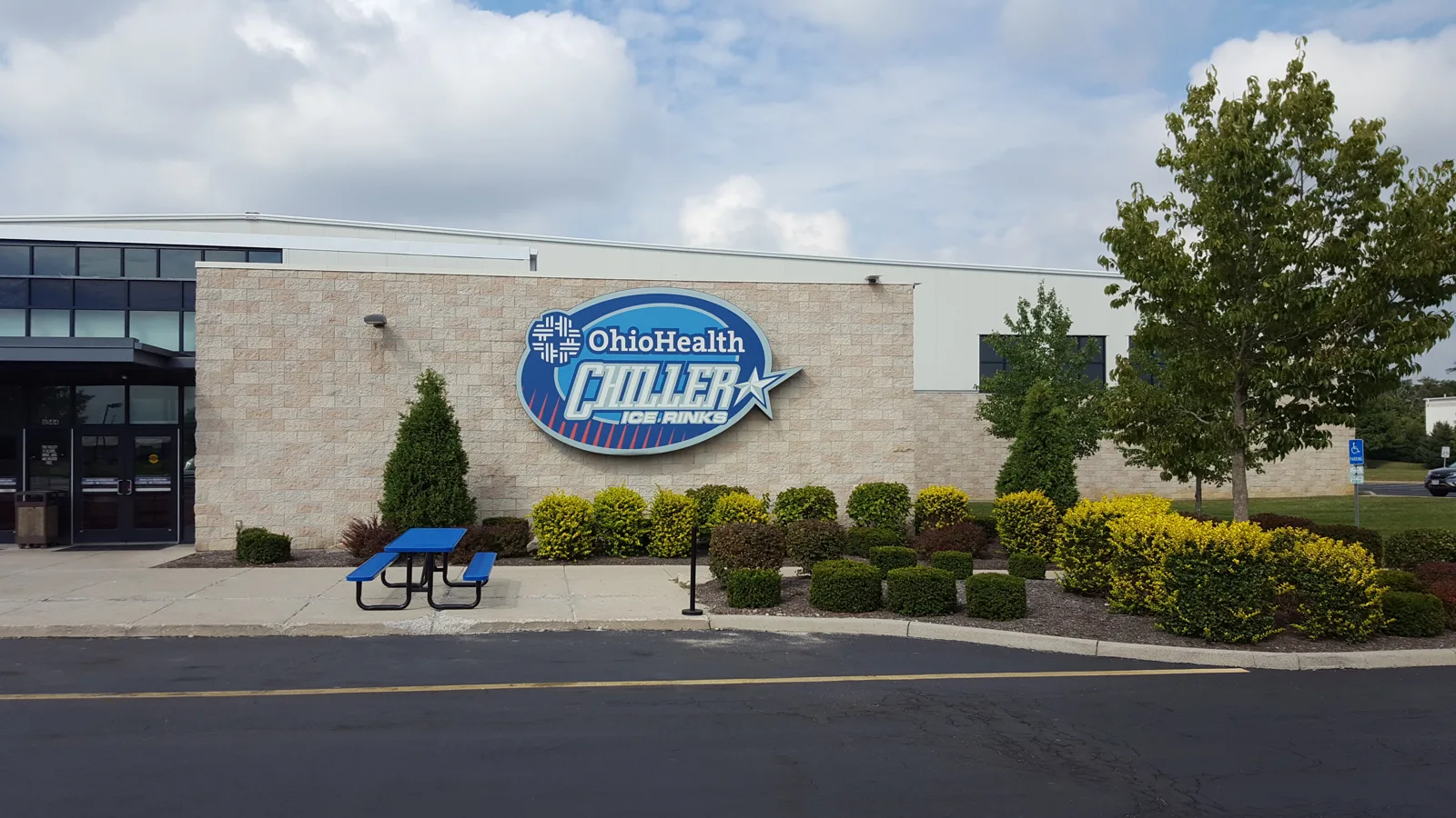 The OhioHealth Chiller Ice Rinks sign on the stone front wall, with landscaped beds and a picnic table by the entrance — OhioHealth Chiller North