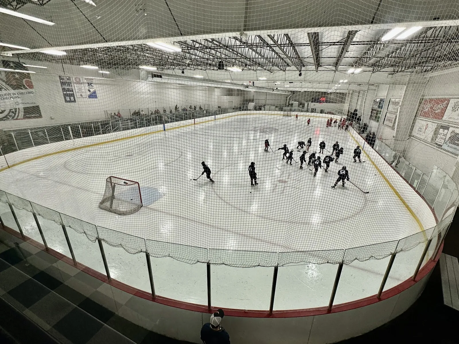 A wide fisheye view of the sheet from beside the boards, a team spread across the ice under a steel ceiling with sponsor boards around it. — OhioHealth Chiller North