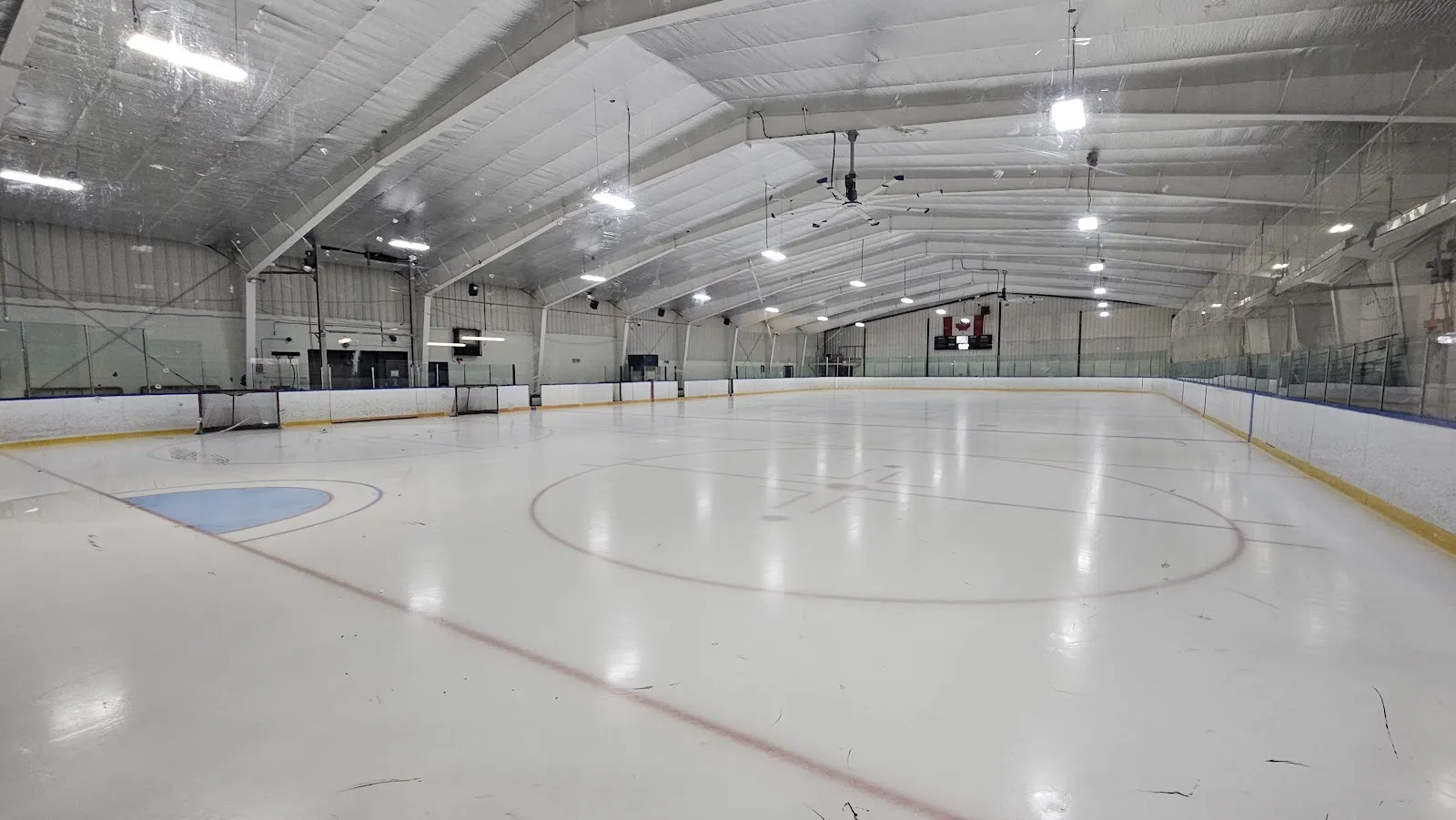 The empty Chippawa ice with a fresh centre circle and red line, under a white-panelled roof with long light rows. — Chippawa Willoughby Memorial Arena