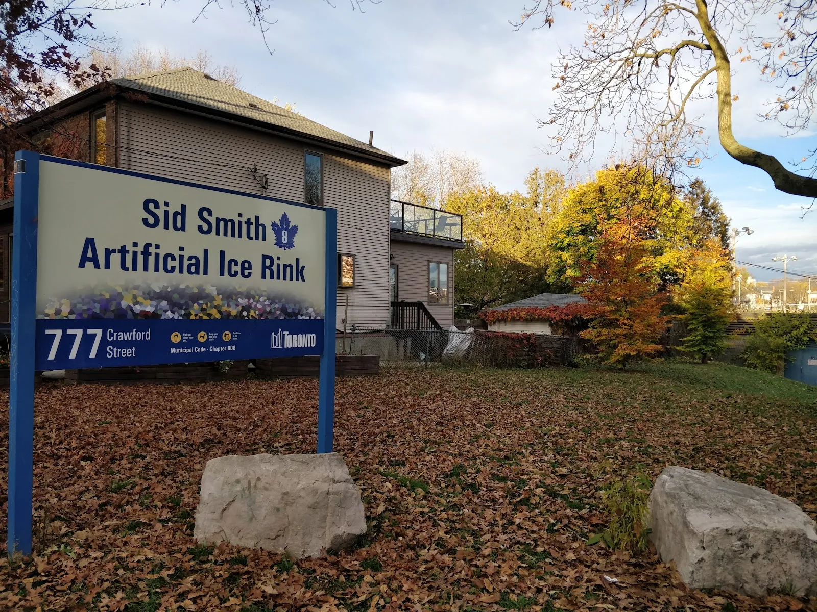 El letrero de la Sid Smith Artificial Ice Rink en 777 Crawford Street, junto a Christie Pits Park, con hojas de otoño y sin personas a la vista — Christie Pits Park Outdoor Ice Rink