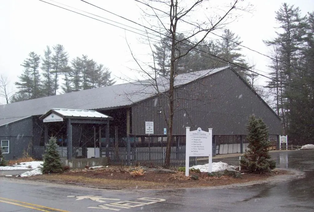 Churchill Rink en Durham: un edificio largo y oscuro con un porche de entrada cubierto, un poste con letrero y árboles sin hojas alrededor en un día gris de invierno. — Churchill Rink at Jackson's Landing
