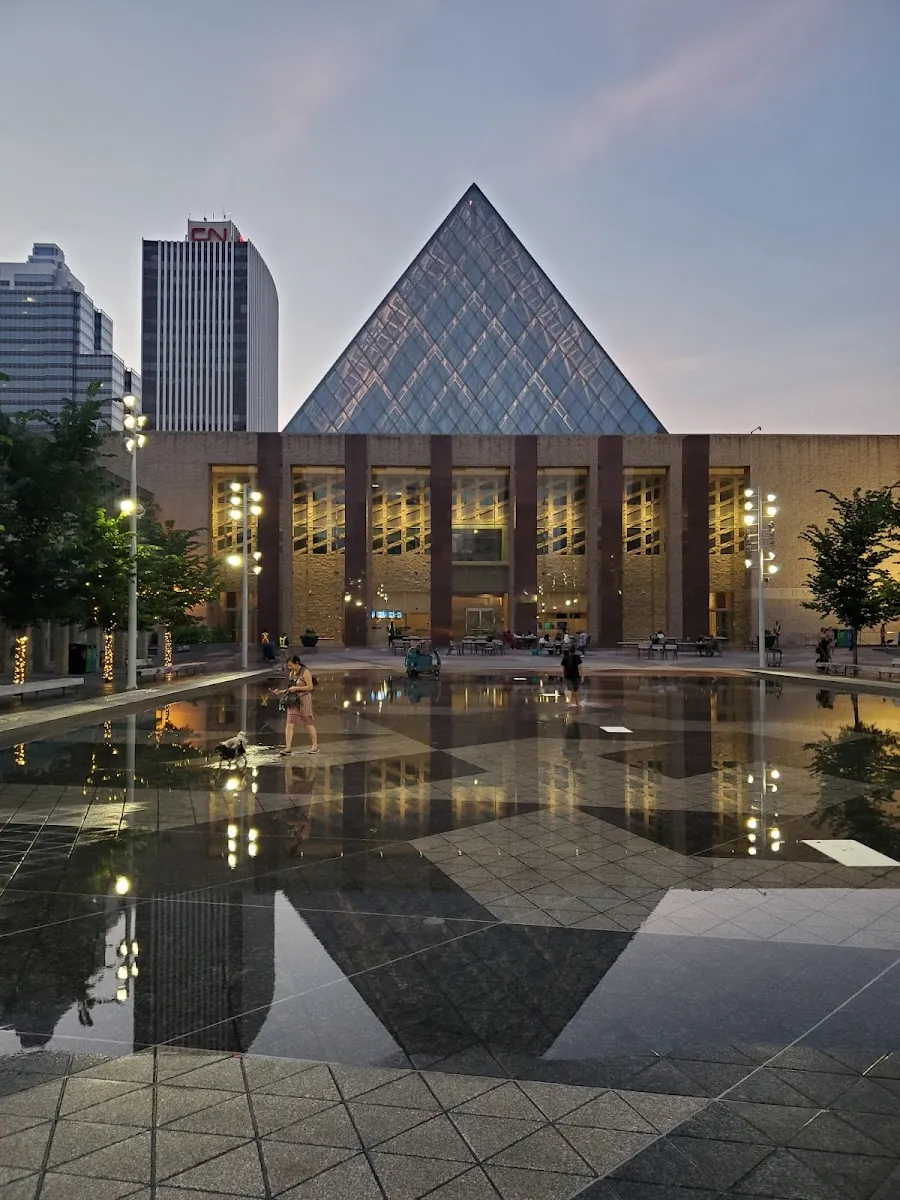 Edmonton City Hall's glass pyramid and the Churchill Square plaza with its water-feature pool at dusk in the warm season, no ice — City Hall Outdoor Ice Rink