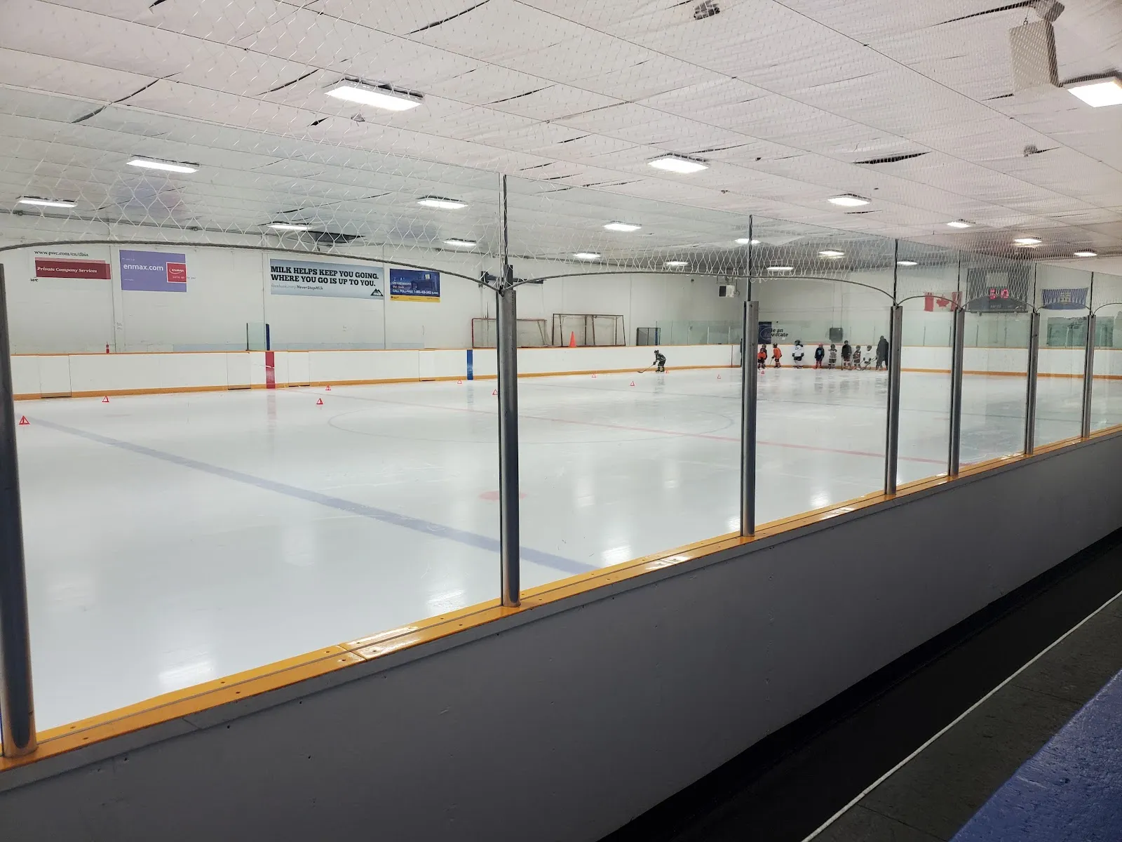 La larga pista Civic de techo bajo, vista desde junto al vidrio, con algunos patinadores en el extremo del fondo. — Civic Ice Centre