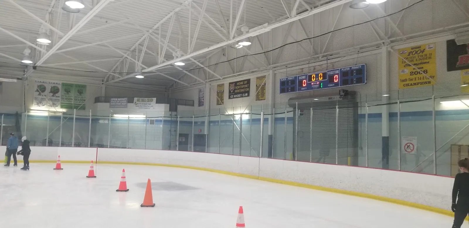 Una de las dos pistas vista desde el hielo, con conos colocados, un marcador azul, una manta Home of Northport Huntington Ice Hockey Club y mantas de campeonatos juveniles en la pared. — Clark Gillies Arena