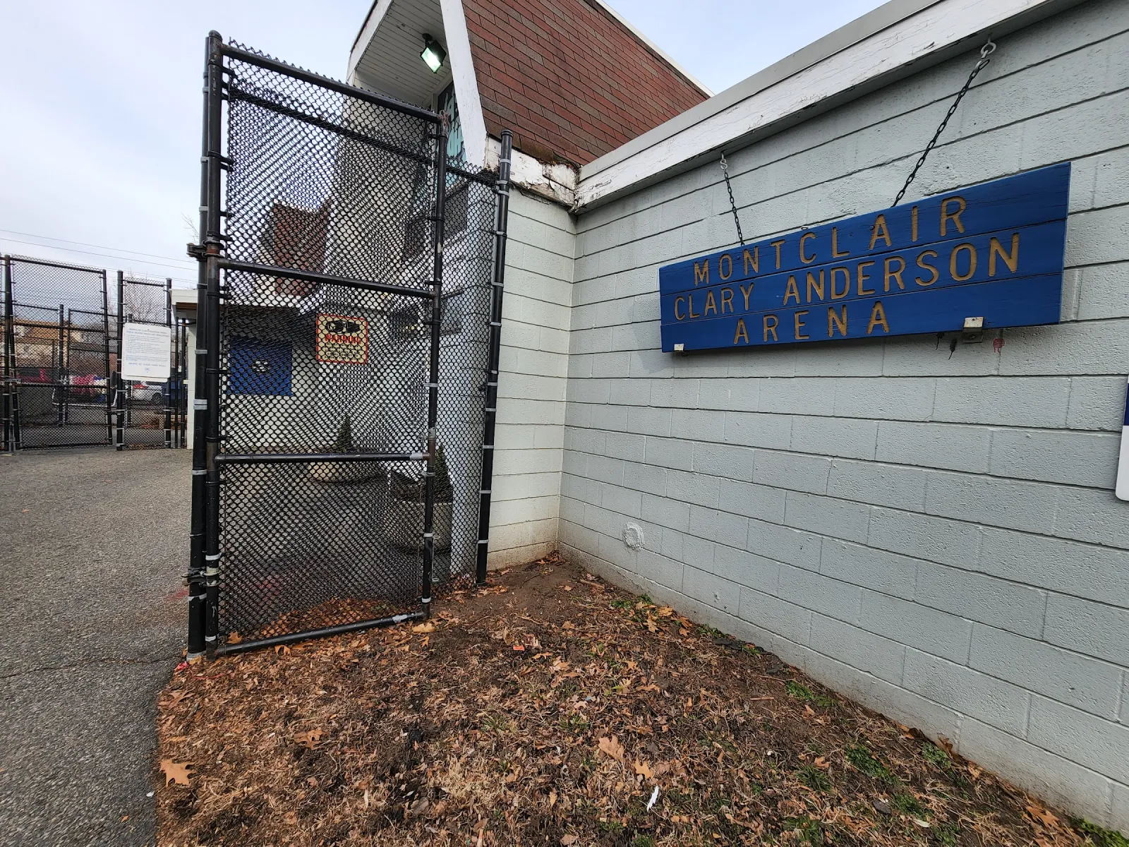 El costado del edificio de la arena con un letrero azul de Montclair Clary Anderson Arena en el revestimiento gris, junto a una reja de malla ciclónica. — Clary Anderson Arena