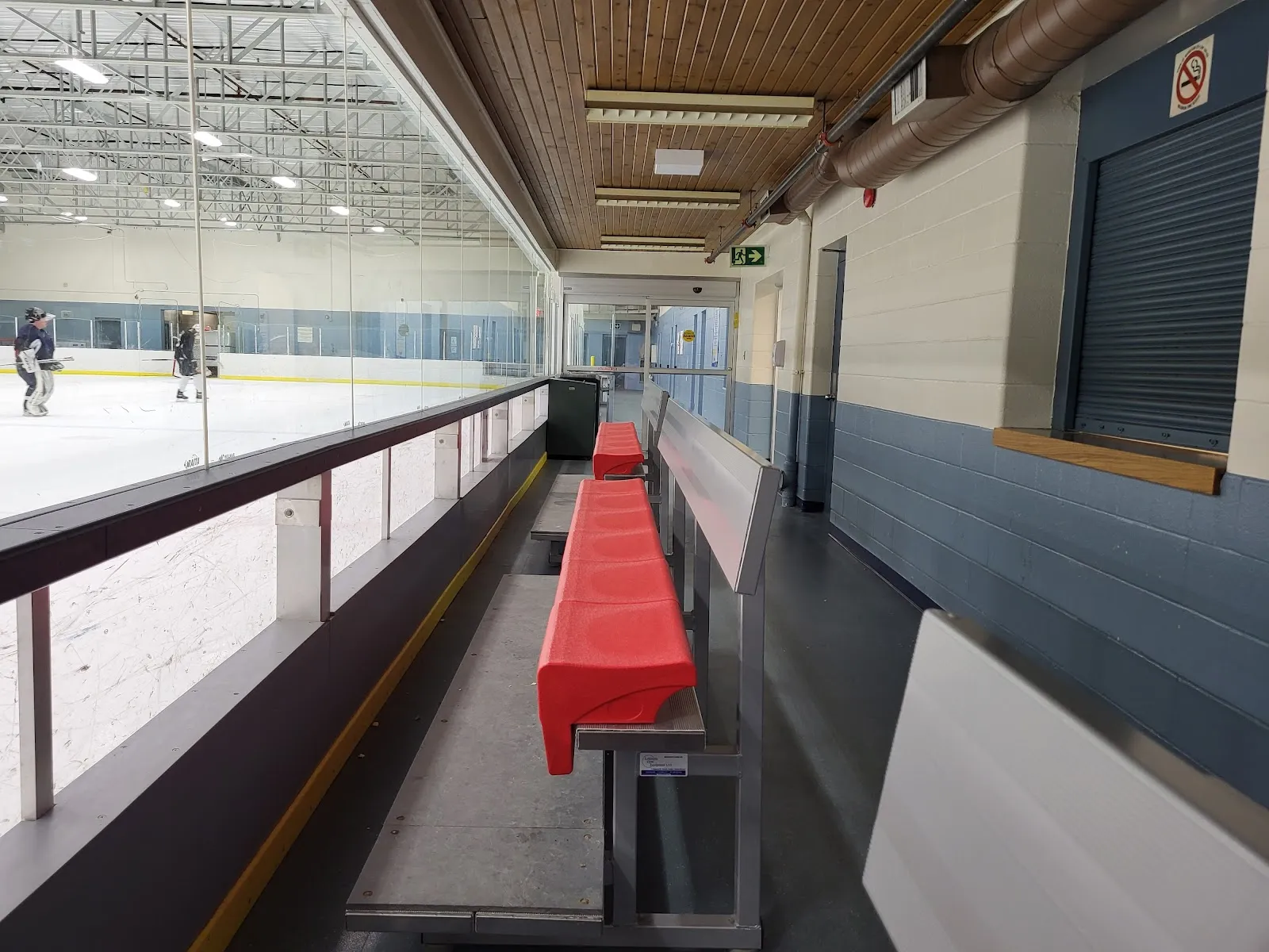 Área de bancas para espectadores junto al cristal, con el hielo y algunos patinadores a lo lejos visibles a la izquierda. — R.J. Clatworthy Arena