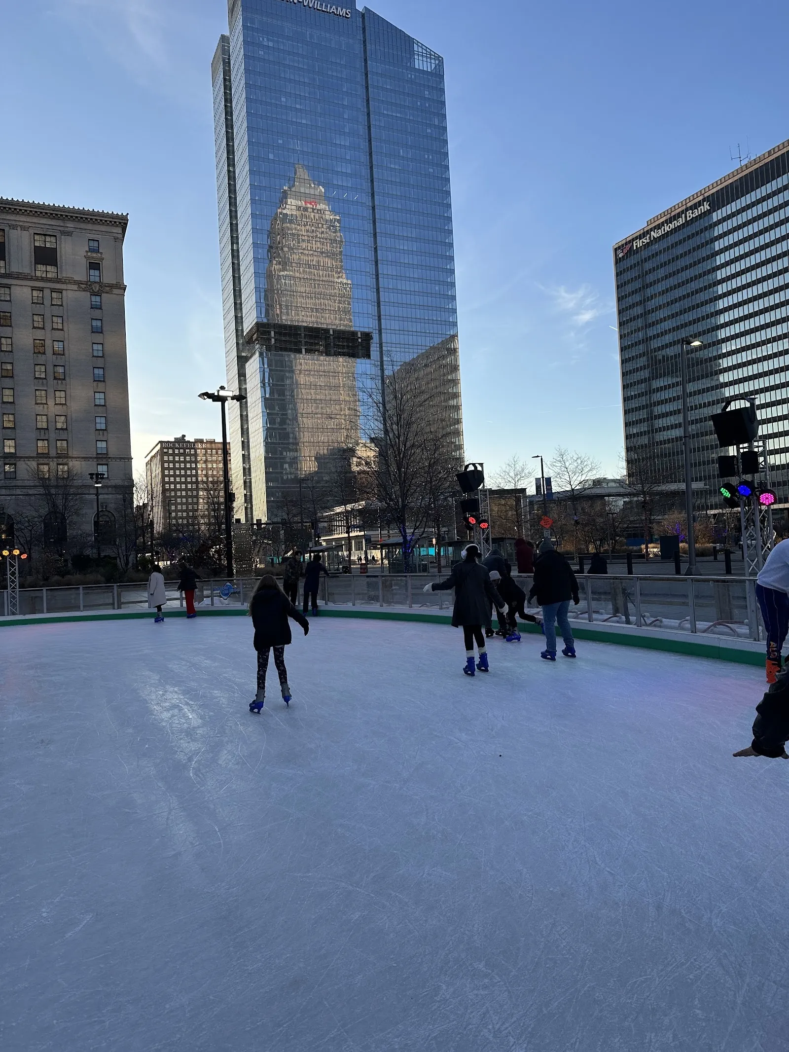 The Public Square rink in the evening, skaters spread across the ice below the glass towers of downtown Cleveland. — Cleveland Foundation Skating Rink