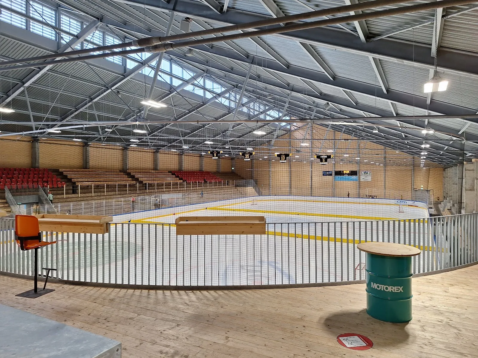 The empty Clientis Arena ice hall with its white boards, glazed roof strip and a timber-framed bench area. — Clientis Arena