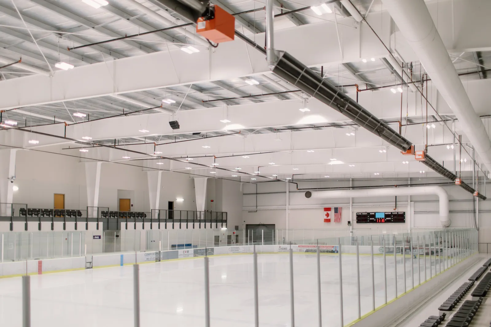 Una pista vacía del Cobourg Community Centre, con cristal sobre las vallas blancas y las armaduras de acero del techo arriba. — Cobourg Community Centre