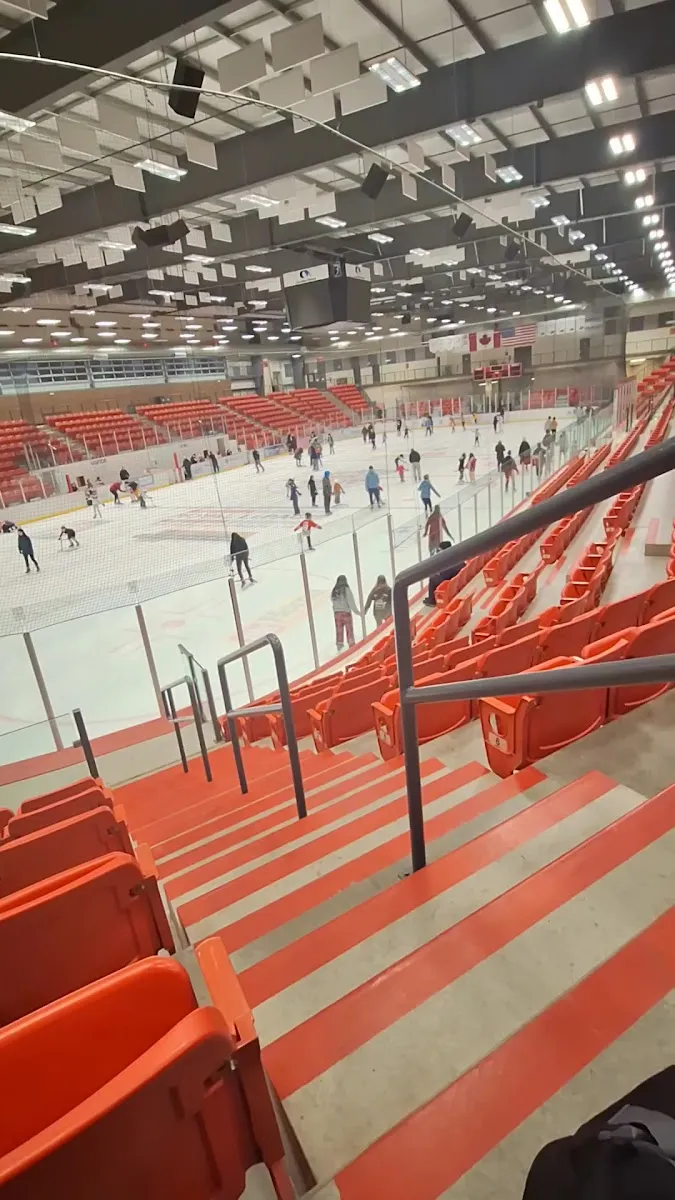 Raked red seating above the Cold Lake Energy Centre arena ice with skaters spread across the surface. — Cold Lake Energy Centre
