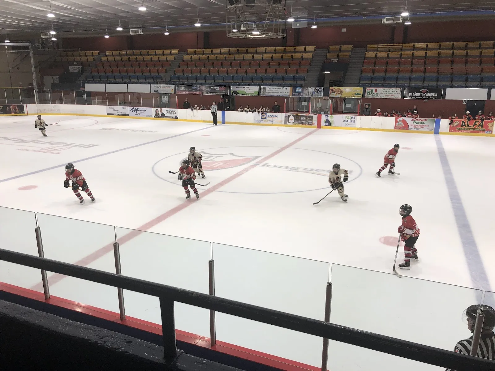 Des patineurs sur la glace au Colisée Jean-Béliveau, avec les gradins de l'aréna derrière. — Colisée Jean-Béliveau