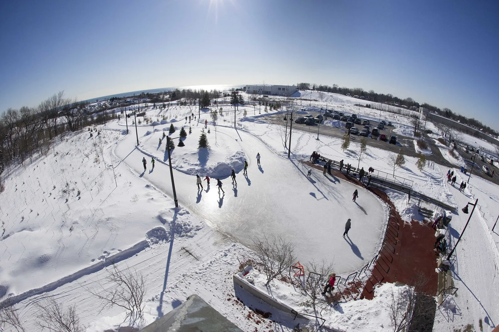Aerial view of the Colonel Samuel Smith Park skate trail in winter, skaters following the curving ice path through the snow-covered park — Colonel Samuel Smith Park Skate Trail