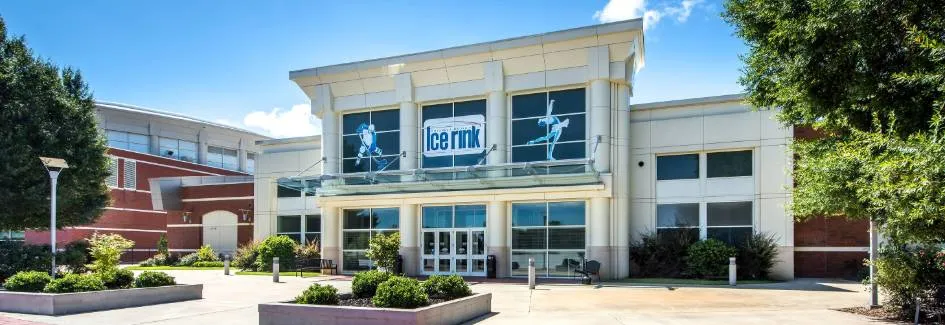 La entrada con frente de vidrio de la pista, con el letrero Ice Rink y gráficos de patinadores sobre las puertas. — Columbus Ice Rink