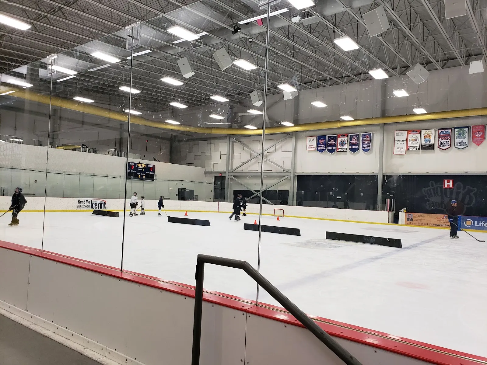 La pista vista sobre las bandas, con banderines de ligas en la pared del fondo y algunos patinadores en el hielo. — Columbus Ice Rink