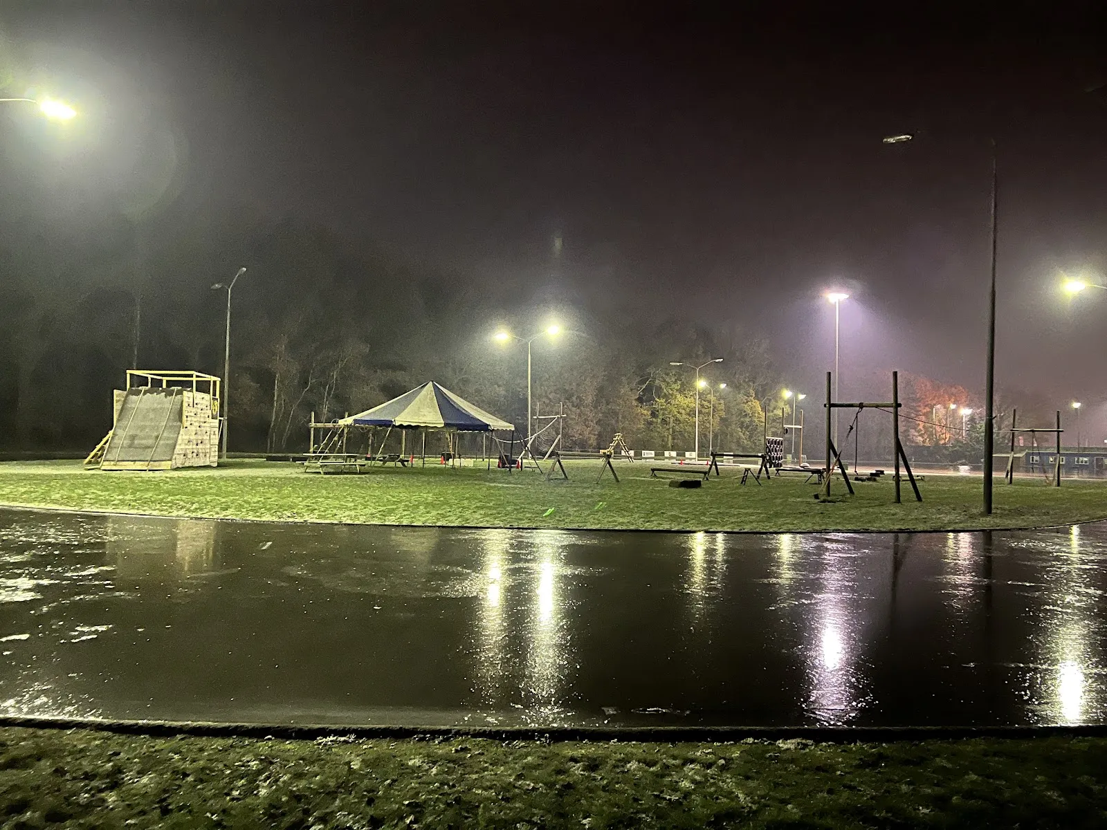 The frozen track at Combibaan Hengelo at night under floodlights, with the park's play equipment and climbing wall on the grass beyond. — Combibaan Hengelo