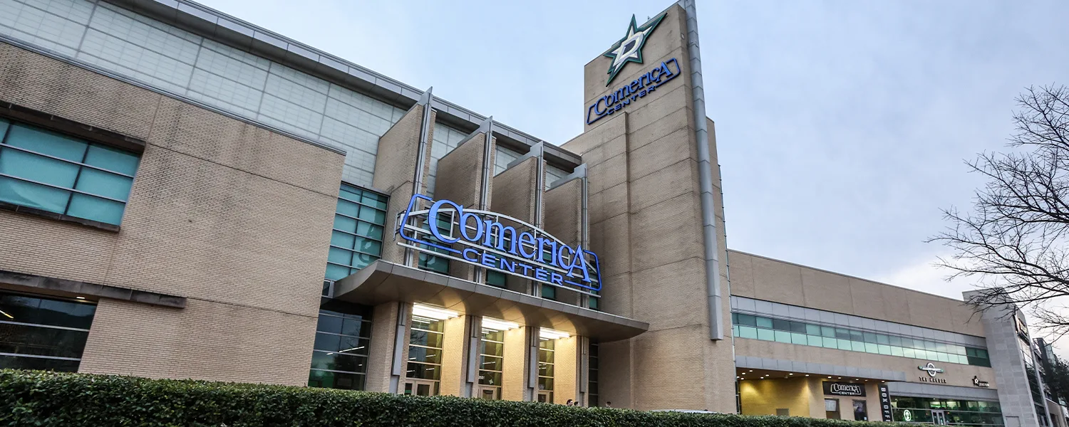 Stone and glass at dusk, the Stars pylon above the door bank — Comerica Center (Frisco)