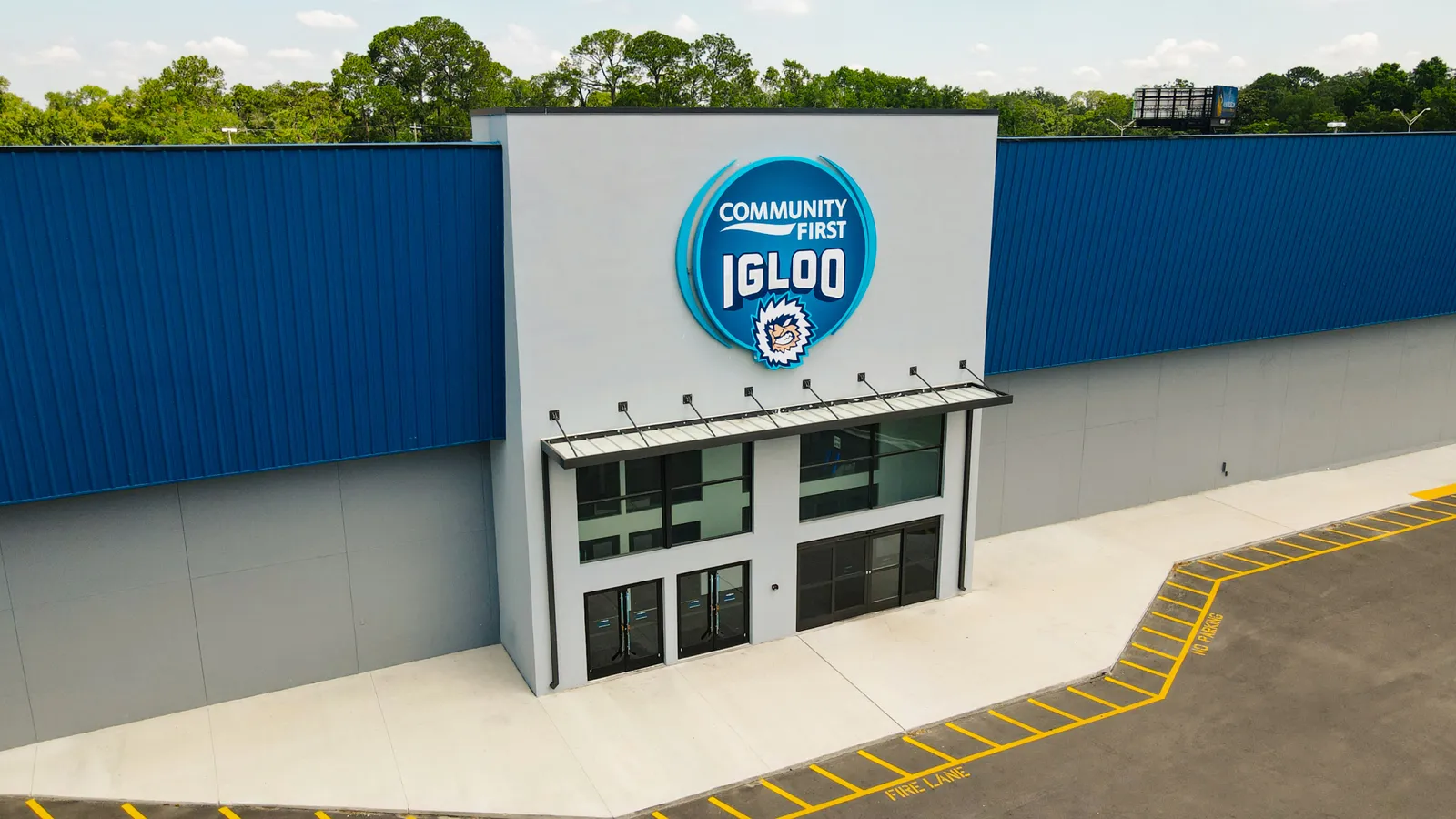 Entrada principal del Community First Igloo, con la fachada metálica azul y gris del edificio y el letrero circular de "Community First Igloo" con su mascota parecida a un oso polar sobre las puertas de vidrio — Community First Igloo