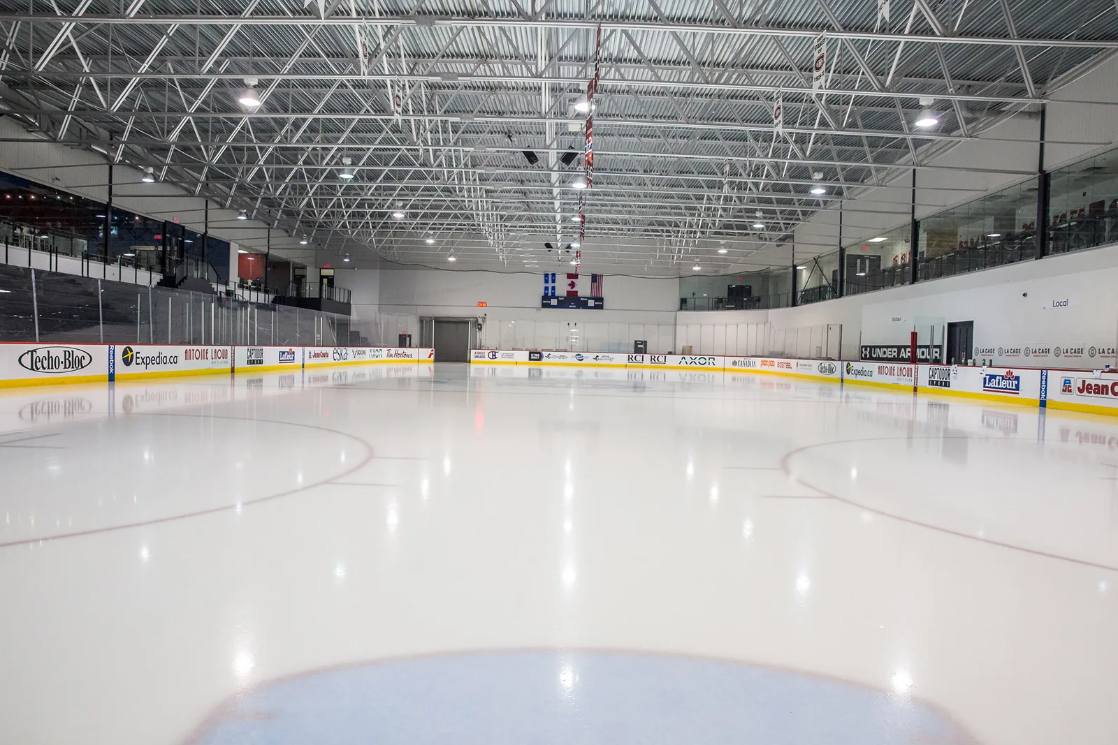 La surface glacée vide du Complexe sportif CN à Brossard, avec les bandes et les gradins le long du côté opposé. — Complexe sportif CN