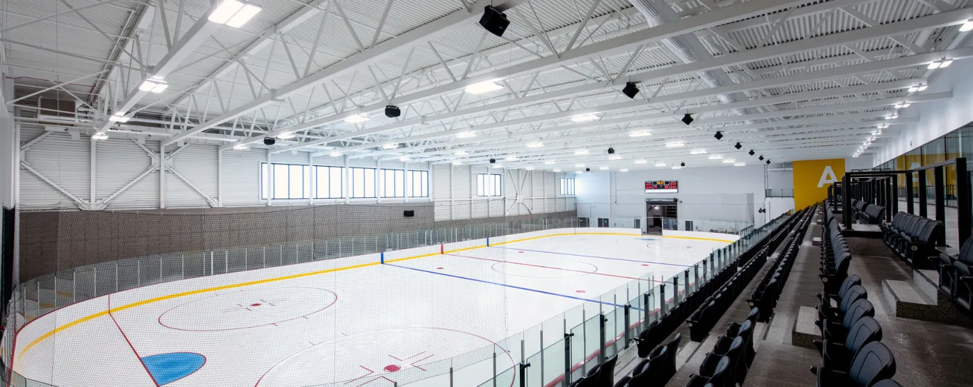 Ice sheet A seen from the stands, with the boards, the black spectator seats and the lit steel roof of the complex. — Complexe sportif Desjardins (Rimouski)