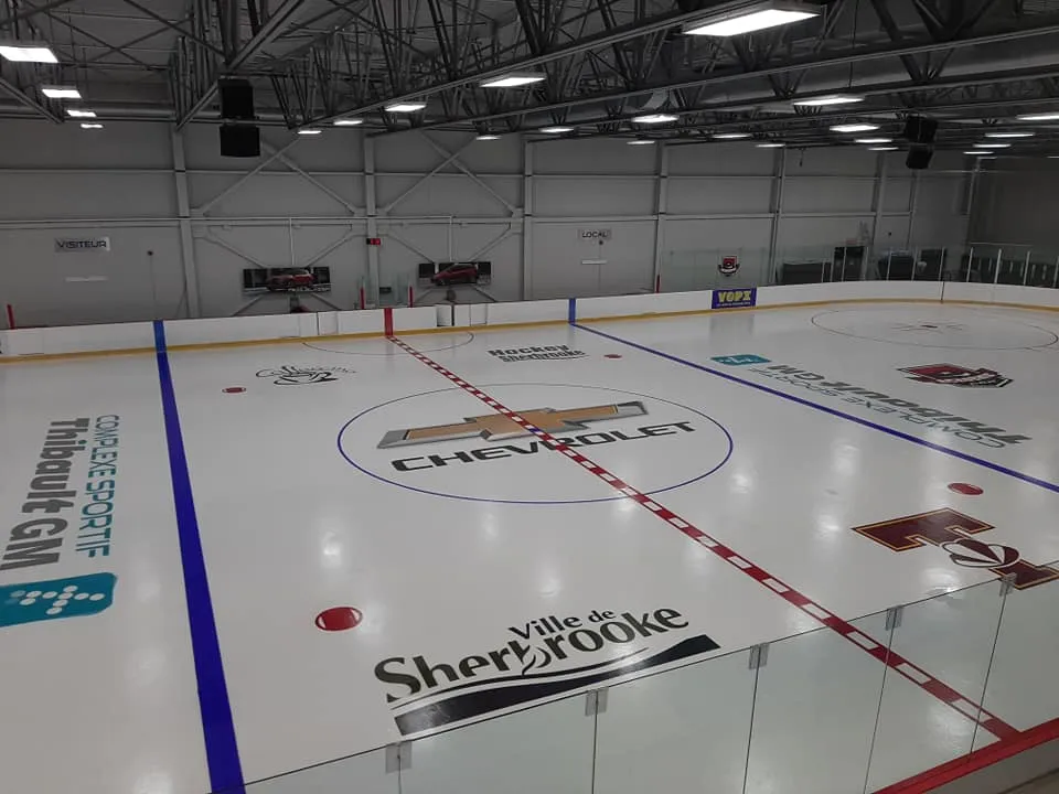 La patinoire Chevrolet vide vue par-dessus la baie vitrée, avec « Complexe sportif Thibault GM » et « Ville de Sherbrooke » peints sur la glace et un logo Chevrolet au centre. — Complexe sportif Thibault GM