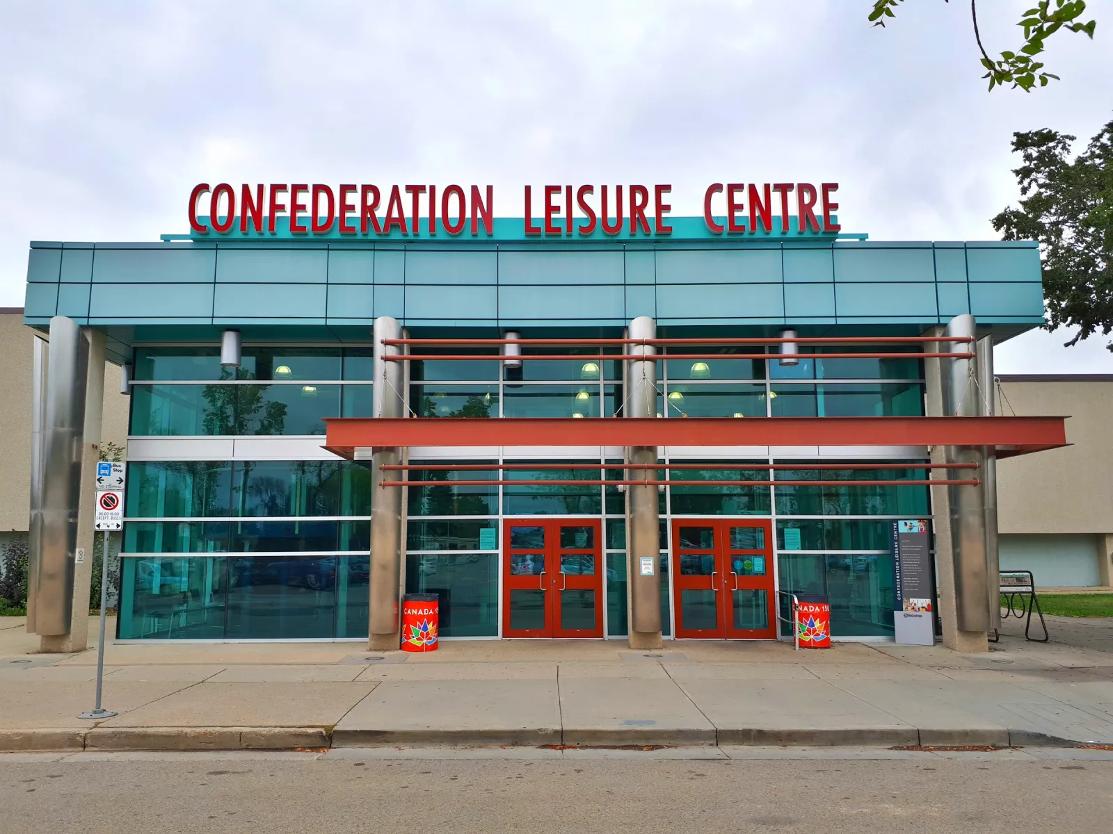 La fachada de vidrio del Confederation Leisure Centre con su nombre en letras rojas a lo largo de la orilla del techo y puertas rojas en la entrada. — Confederation Arena