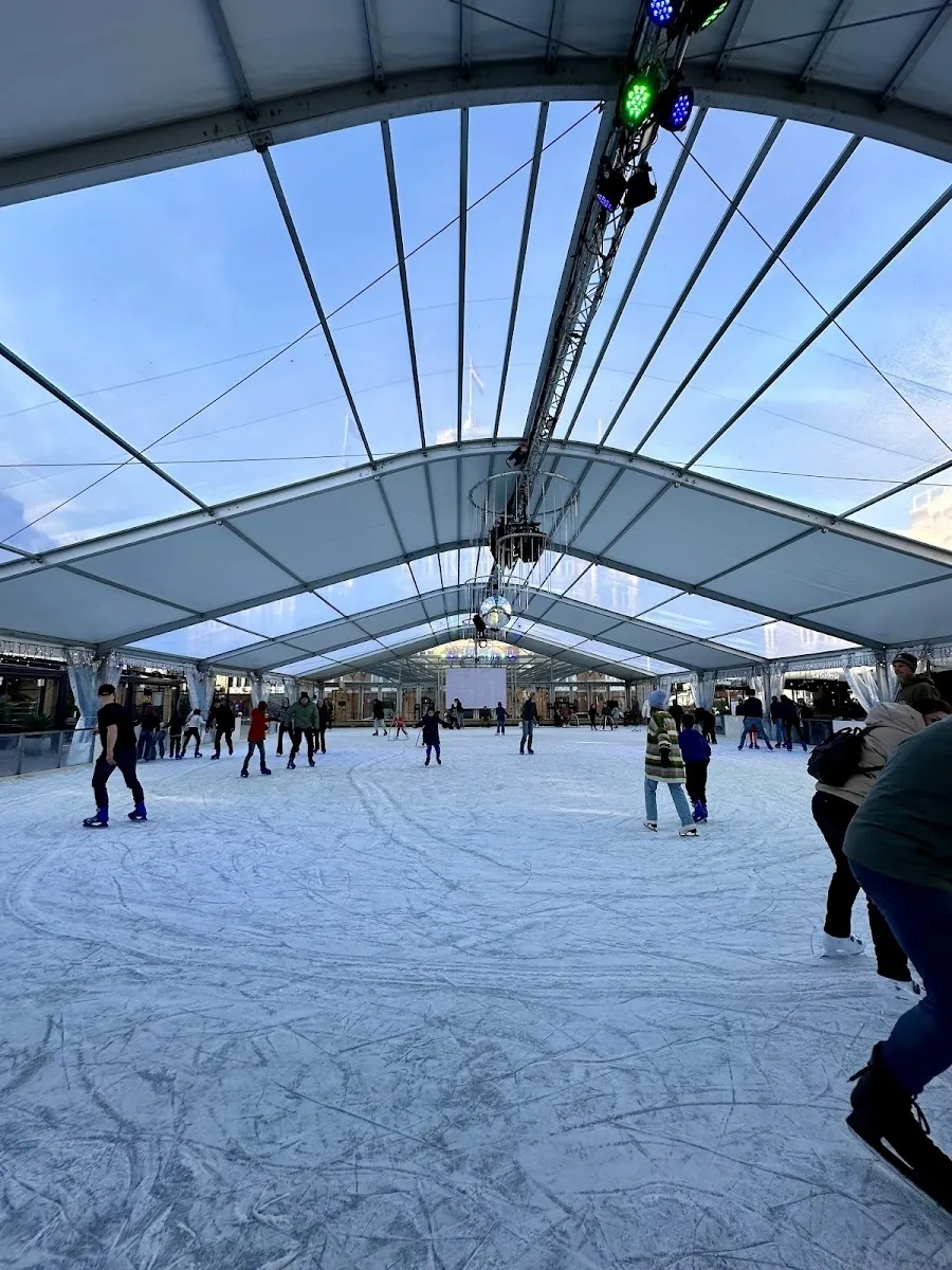 De overdekte ijsbaan van Cool Event Scheveningen onder het doorschijnende dak, met schaatsers op het ijs en een kerstboom ernaast. – Cool Event Scheveningen