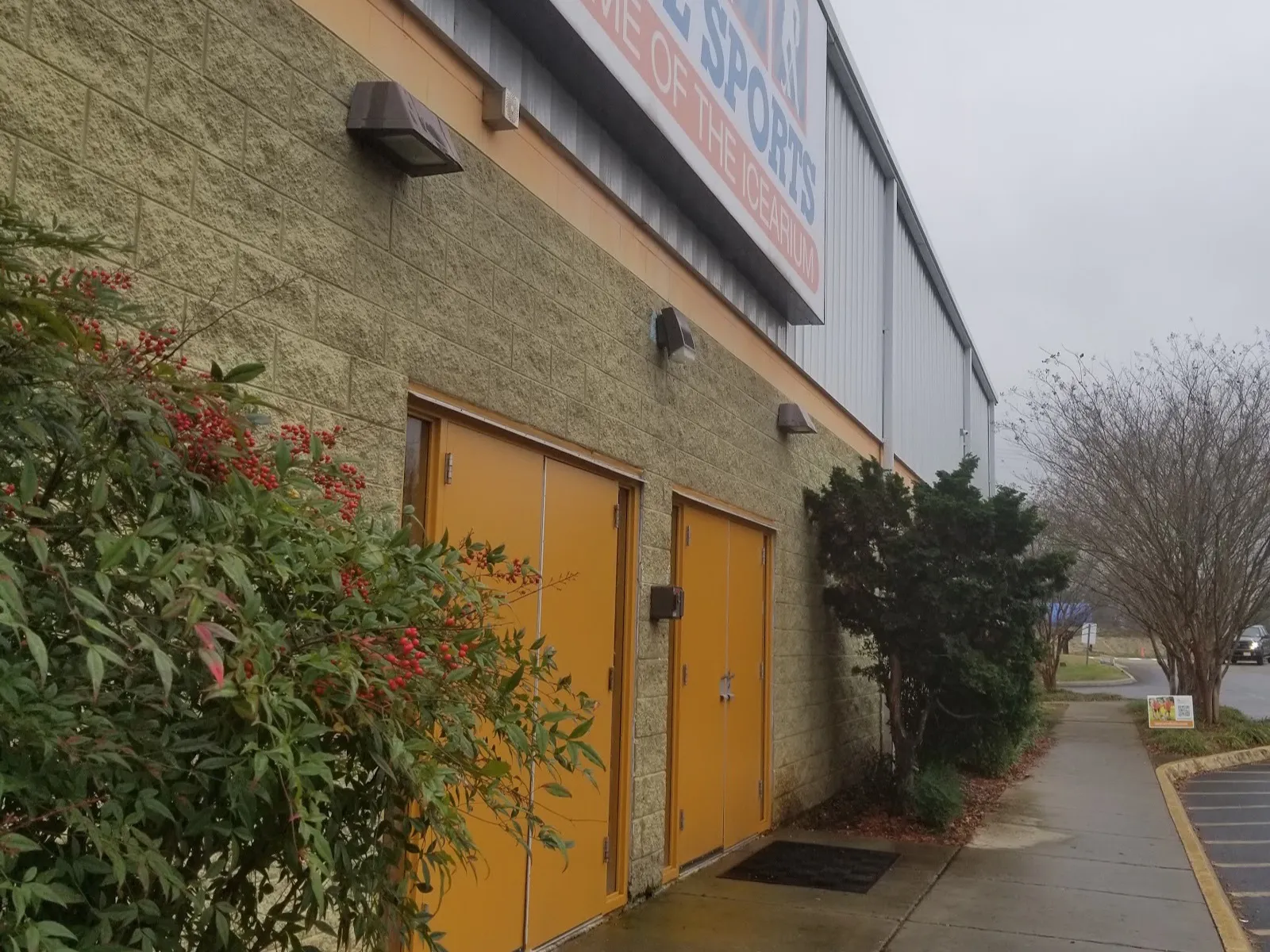 El letrero de Cool Sports, Home of the Icearium, a lo largo del muro lateral de metal y bloques del edificio, sobre las puertas de servicio naranjas — Cool Sports