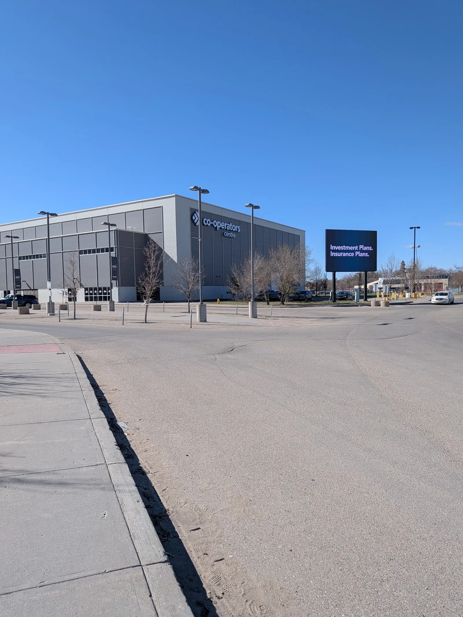 The Co-operators Centre's long grey glass-and-metal facade with its blue name sign above the entrance, seen across a wide empty car park. — Co-operators Centre