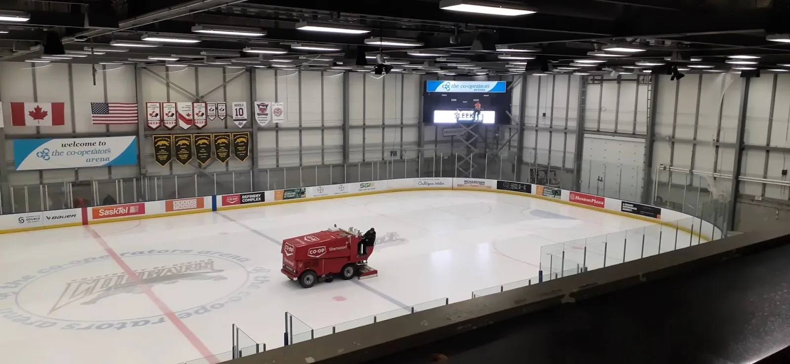 The Co-operators Arena rink from the upper concourse, a resurfacer crossing the logo at centre ice below banners and flags — Co-operators Centre