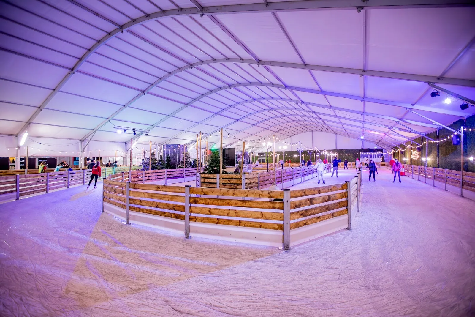 The ice rink under the marquee at Cork On Ice at Marina Market, lit in purple, with skaters on the ice and festive decorations around the sides. — Cork On Ice (Marina Market)