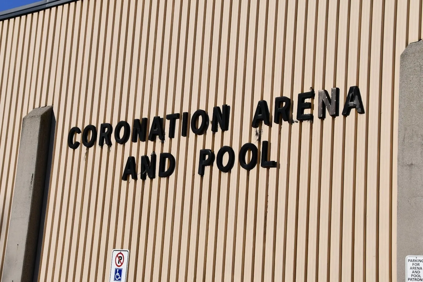 The words Coronation Arena and Pool in black letters on the building's ribbed tan wall between concrete piers. — Coronation Arena (Hamilton)