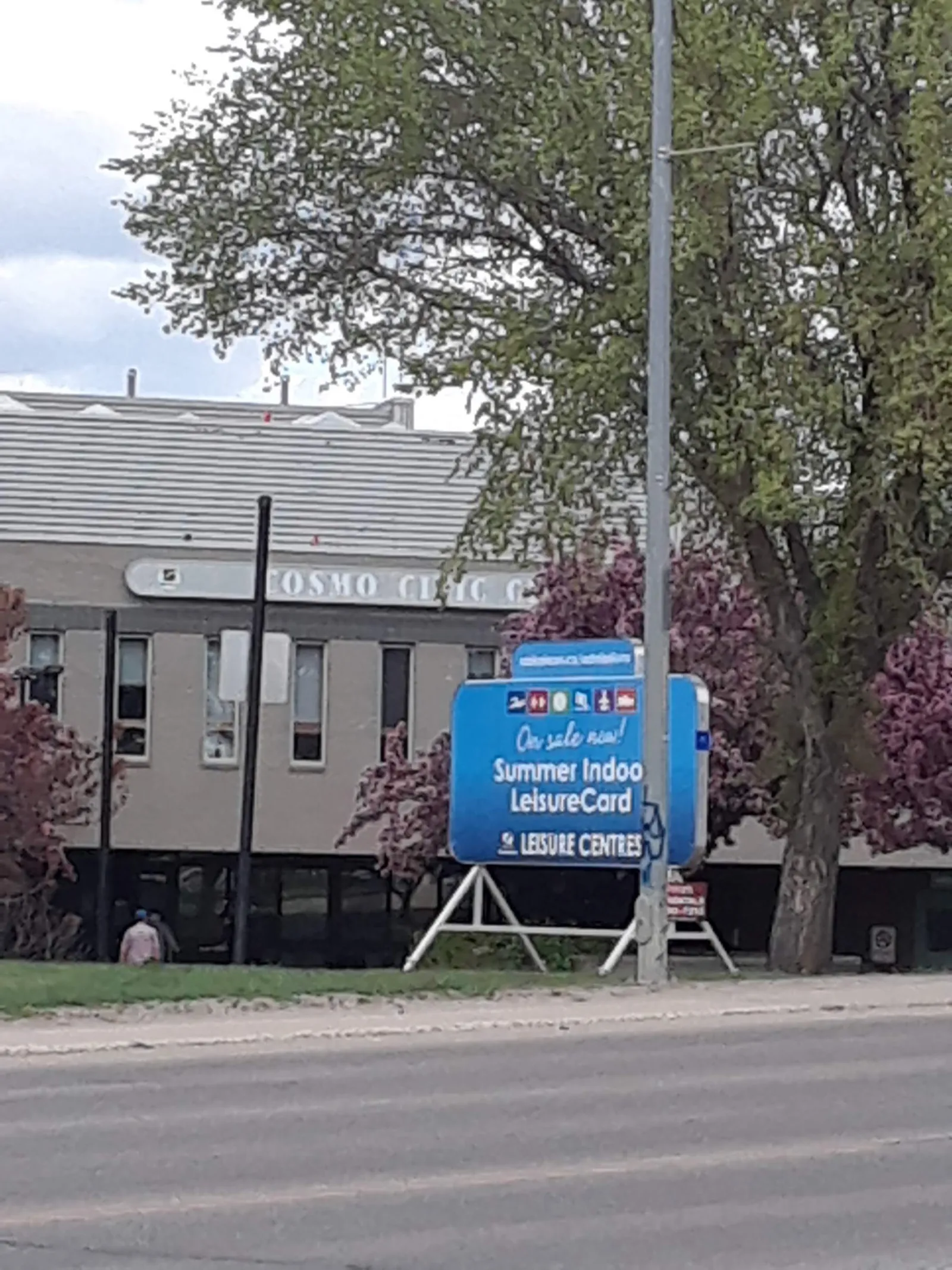 The Cosmo Civic Centre from Laurier Drive in spring, its name on the flat-roofed building partly behind a flowering tree. — Cosmo Arena
