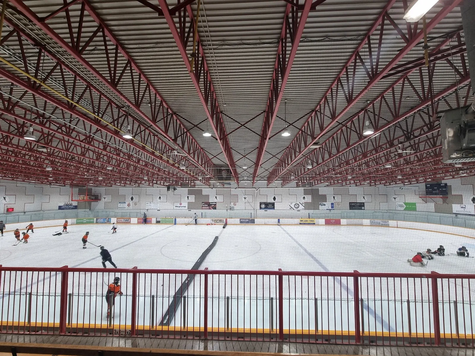 The arena seen from a red-railed upper walkway, a few skaters spread across the sheet below a red-trussed roof. — Cosmo Arena