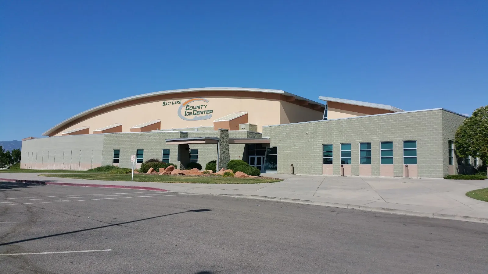 The entrance side of the building from the parking lot, with the Salt Lake County Ice Center sign on the curved roofline above a low block wing. — County Ice Center