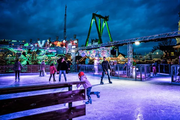 Skaters on the Cranger Weihnachtszauber ice rink in Herne, lit in blue and purple, with the fairground rides behind. — Cranger Weihnachtszauber Echt-Eisbahn