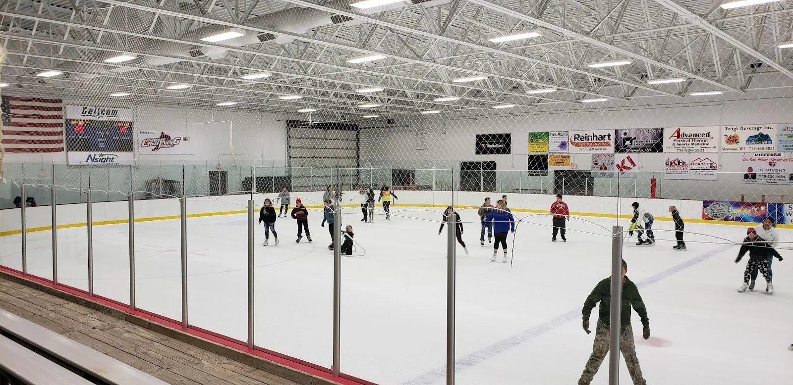 A public skating session on the indoor ice sheet at Crawford Center, skaters across the ice at a distance, glass above the boards and a row of sponsor boards. — Crawford Center