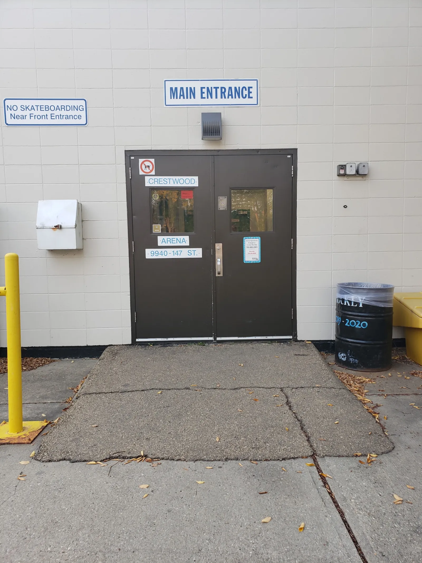 The arena's main entrance from outside: brown double doors lettered Crestwood Arena, 9940 147 St, under a blue Main Entrance sign on a white block wall. — Crestwood Arena