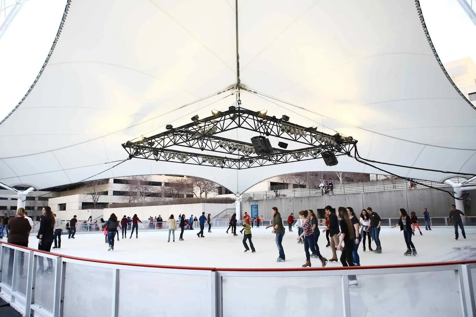 La Ice Terrace bajo su toldo blanco tensado, con patinadores repartidos alrededor de la pista ovalada detrás de un barandal blanco. — Crown Center Ice Terrace