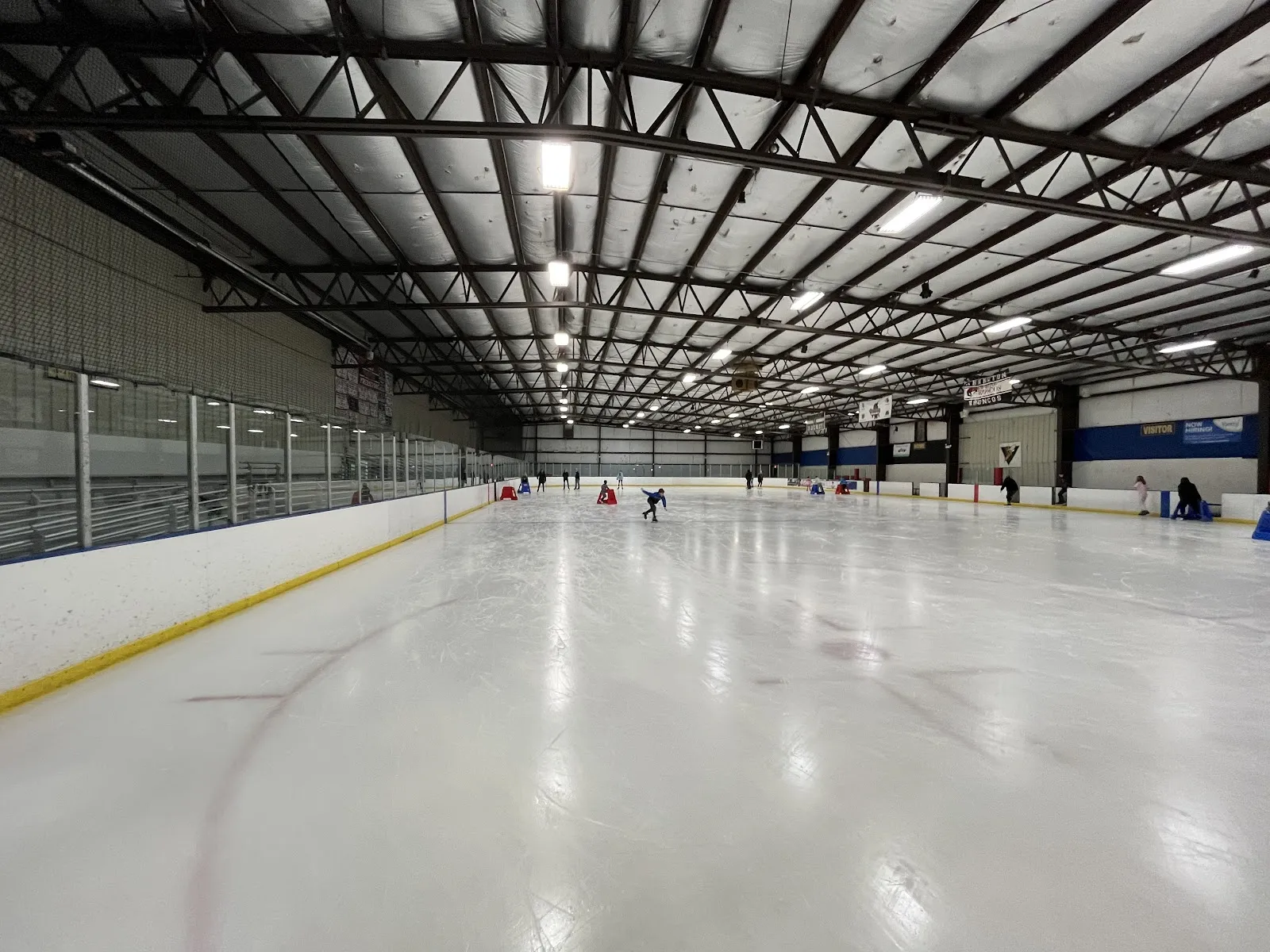 Wide view down the length of one ice sheet from ice level, bleachers and team banners along the boards, a single skater near center ice — Crystal Ice House (Crystal Lake)