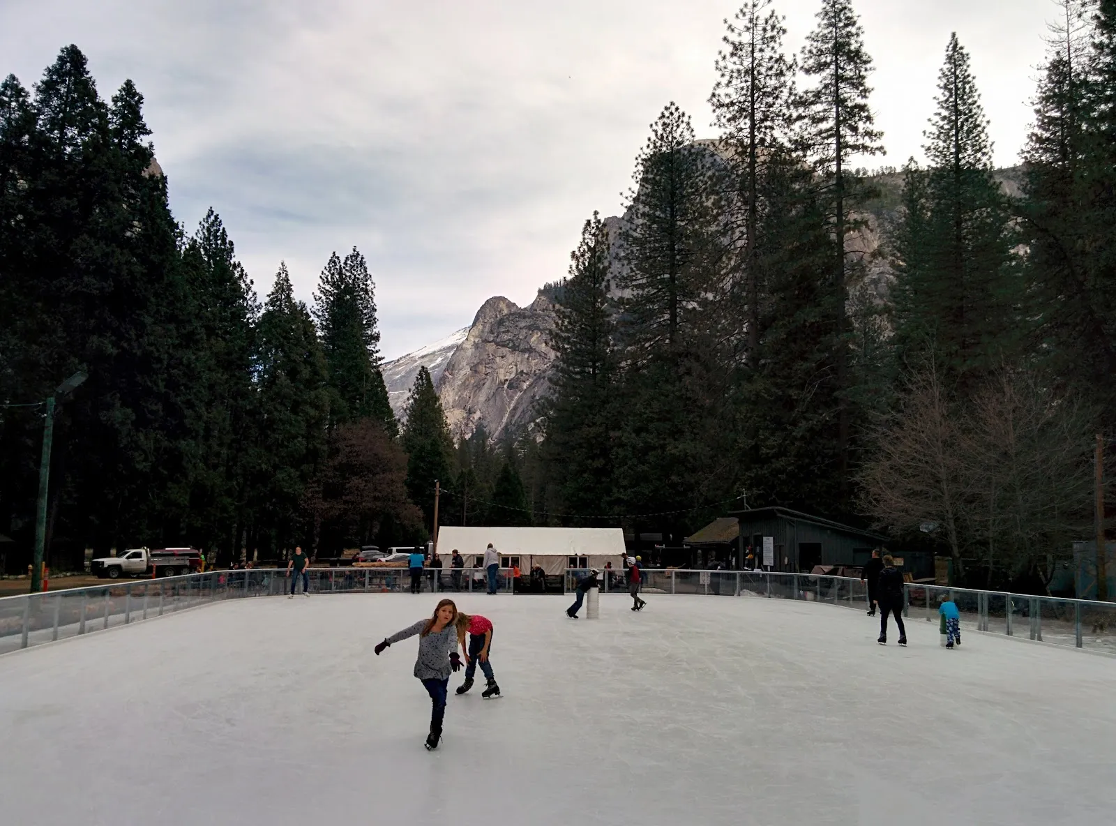 Skaters on the Curry Village rink with Half Dome rising behind the trees — Curry Village Ice Rink