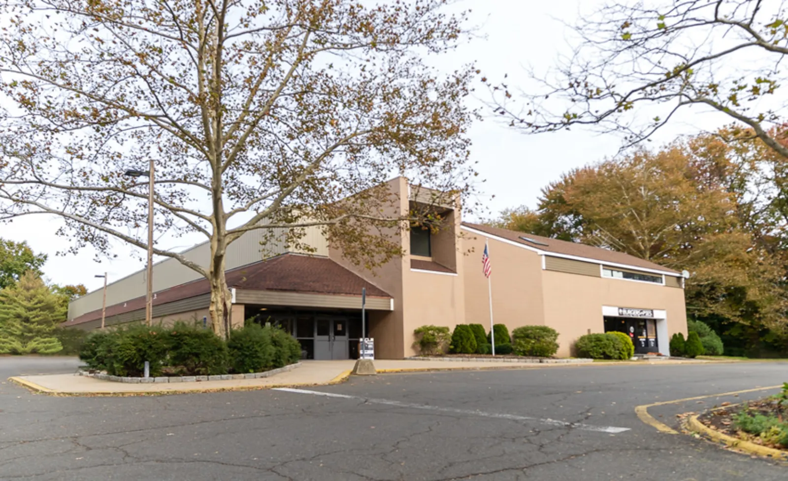 Front entrance and facade of Darien Ice House, a tan brick building with a red-trimmed roofline, glass entry doors, and a flagpole in the parking lot. — Darien Ice House