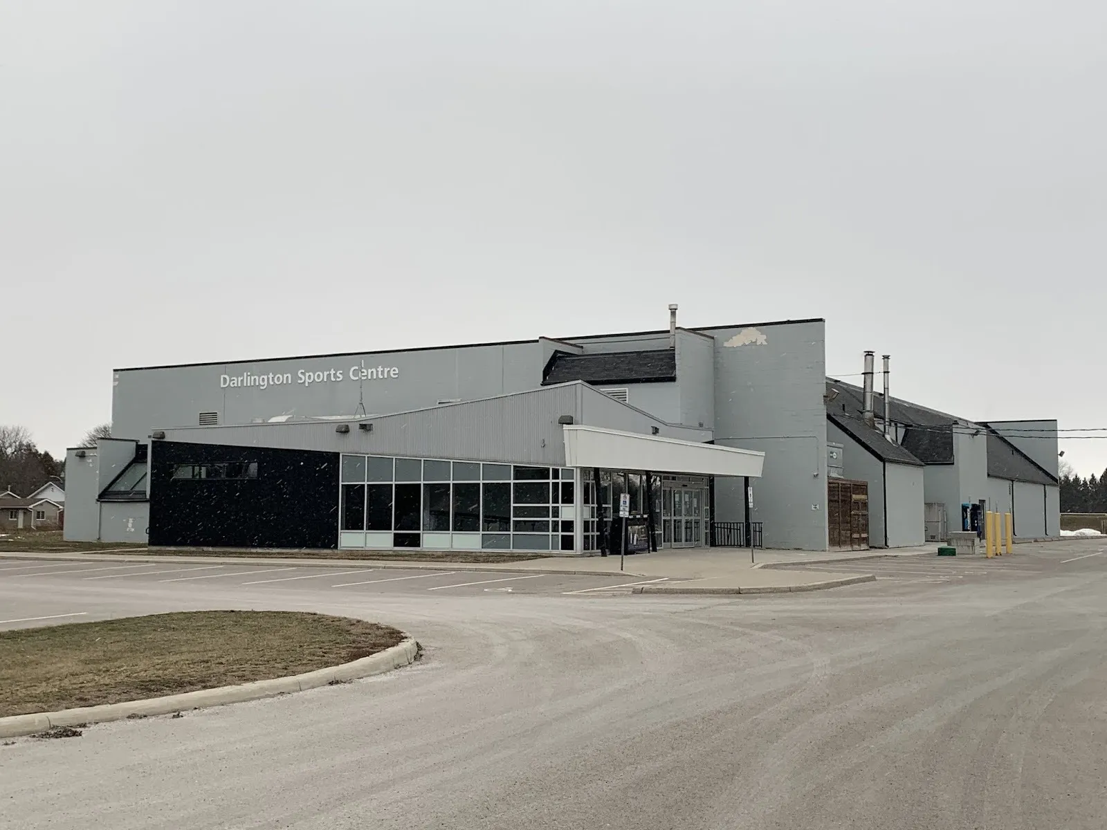 The Darlington Sports Centre, a pale grey arena lettered with its name over a glass entrance with a white canopy, seen across the lot. — Darlington Sports Centre