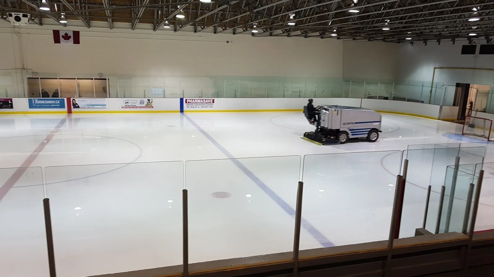 The Darlington Sports Centre ice pad from behind the glass while the resurfacer finishes a flood, with sponsor boards along the far end. — Darlington Sports Centre