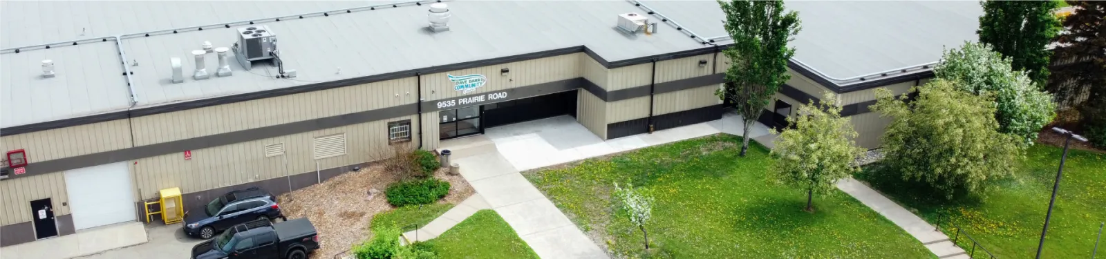 La entrada del Dave Barr Community Centre vista desde el aire, con su logo sobre 9535 Prairie Road y pasto y árboles al frente. — Dave Barr Community Centre